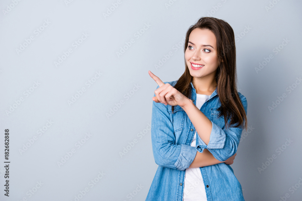Advertisement concept. Successful caucasion woman with beaming smile on grey background is pointing with her index finger and looking on empty copy space Advertisement concept. Successful caucasion woman with beaming smile on grey background is pointing with her index finger and looking on empty copy space
