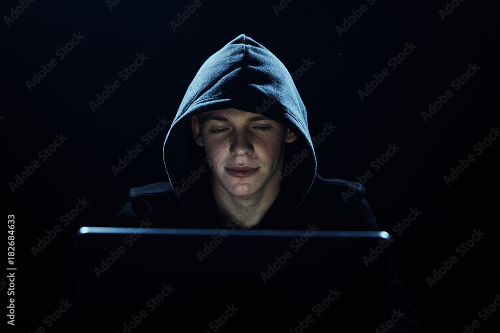 young man sits behind laptop, black background, hacker, technology young man sits behind laptop, black background, hacker, technology