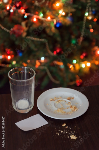 empty glass from milk and crumbs from cookies for Santa Claus under the Christmas tree with lights, close-up