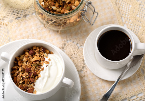 Healthy breakfast: Greek yogurt with homemade granola in a white bowl, a cup of coffee