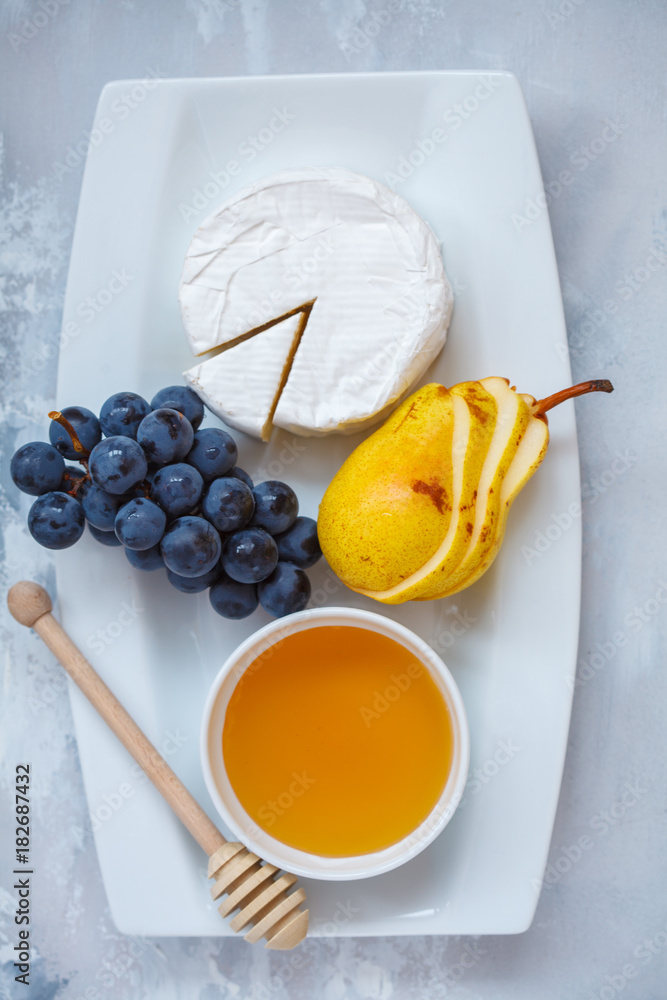 Cheese brie (camembert) with honey and fruits on a white plate.