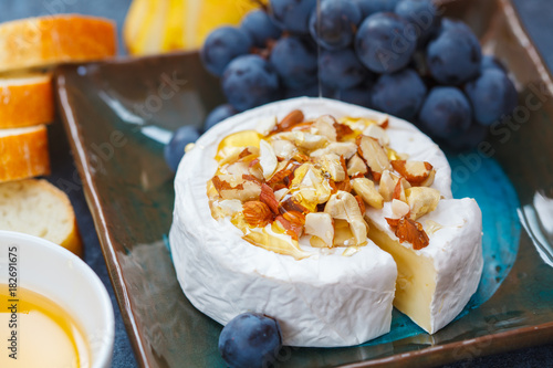 Brie cheese (camembert) with honey, nuts, baguette and fruit on a slate board.