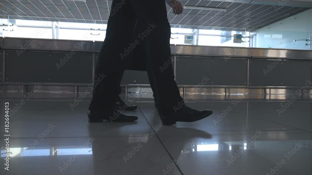 Feet of two businessmen walking at terminal of airport. Legs of business men stepping together. Colleagues going indoors. Slow motion Low angle of view Close up Feet of two businessmen walking at terminal of airport. Legs of business men stepping together. Colleagues going indoors. Slow motion Low angle of view Close up