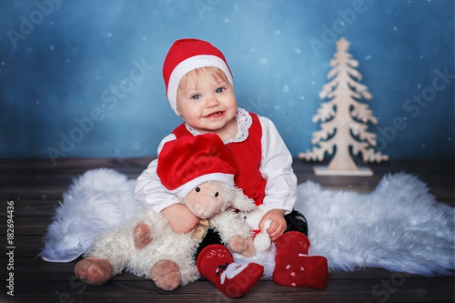 Baby girl in Santa hat sitting in a Christmas interior with toys.
