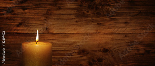 Burning candle in front of rustic wooden wall