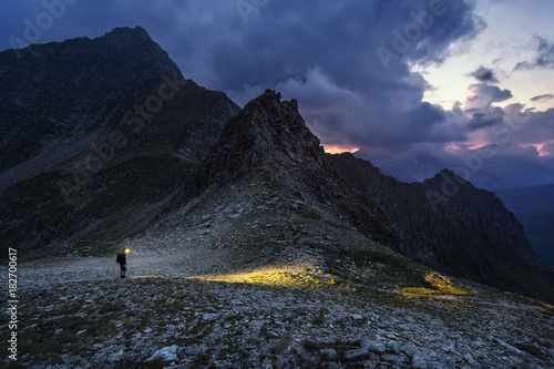 Hiker passes over the Gliederscharte mountain gorge at nightfall, Pfitsch, Part of the long distance hiking trail from Munich to Venice, South Tyrol, Italy photo