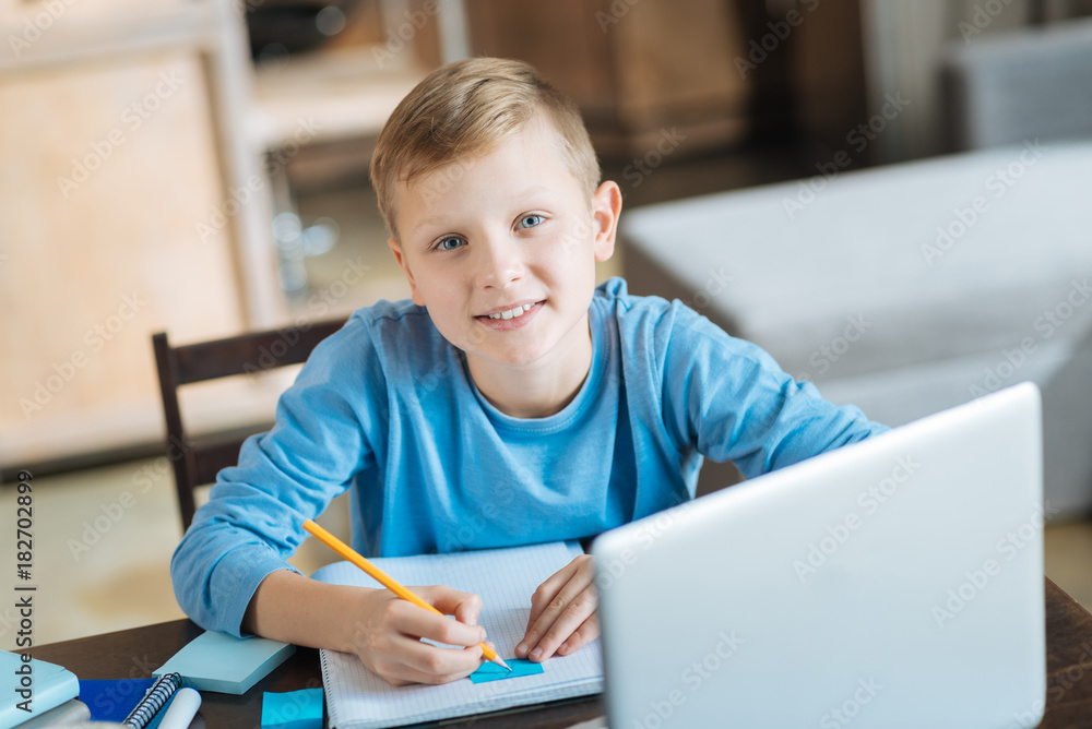 School system. Happy delighted nice boy sitting in front of his notes and studying while doing his home task School system. Happy delighted nice boy sitting in front of his notes and studying while doing his home task