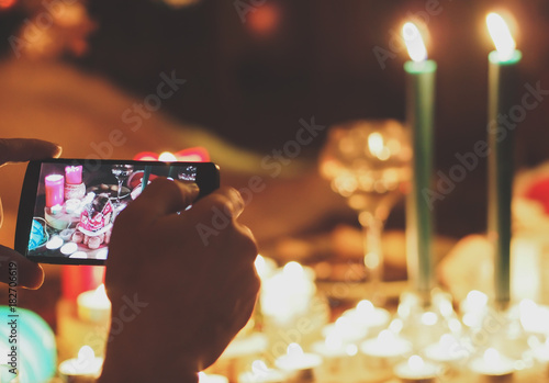 Photography Human hand holding mobile phone and taking picture of New Year accessories, candles and food on the table