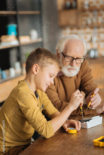 Being smart. Nice positive joyful boy smiling and holding a screwdriver while fixing an electronic device