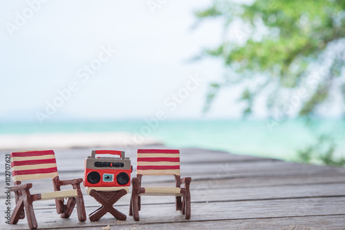 Fototapeta Naklejka Na Ścianę i Meble -  Miniature radio on a table and beach chair with sea background.