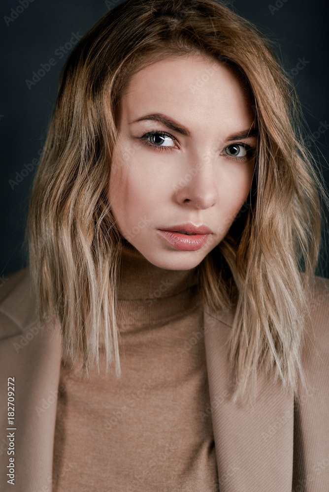 Naklejka premium Portrait of young attractive pretty blonde woman in the beige jacket on the dark background 