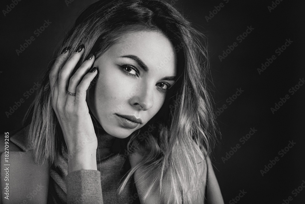 Black and white portrait of young attractive pretty blonde woman in the jacket, leather shirt, gaiters, patent shoes on the dark background Black and white portrait of young attractive pretty blonde woman in the jacket, leather shirt, gaiters, patent shoes on the dark background