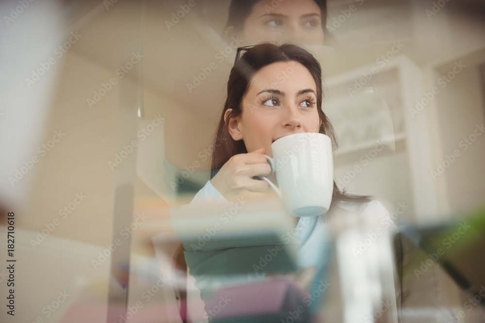 Woman drinking coffee while sitting by glass table Woman drinking coffee while sitting by glass table