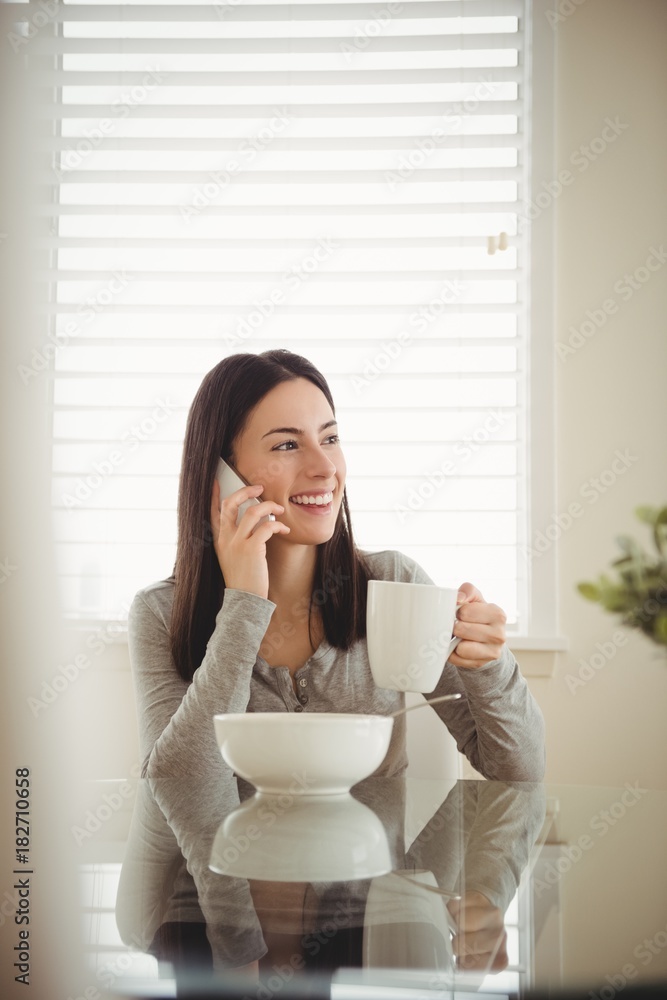 Smiling woman talking on mobile phone while eating breakfast Smiling woman talking on mobile phone while eating breakfast