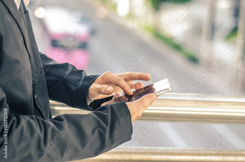 Close up of young business man using mobile smartphone blurry city background.