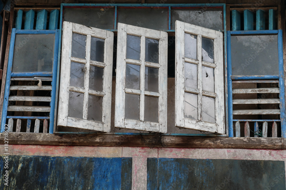 Old and faded wooden blue and white windows, traditional facade of thai house with open window