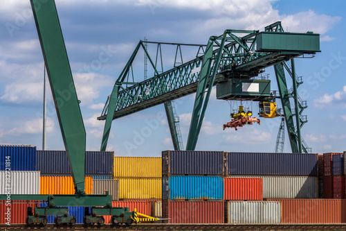 Grüner Lastenkran schwebt über gestapelten Containern im Containerhafen