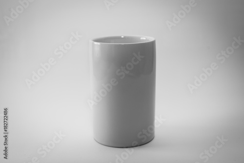 Clean white cup with no handle on a grey/white background. Minimalist and abstract design approach