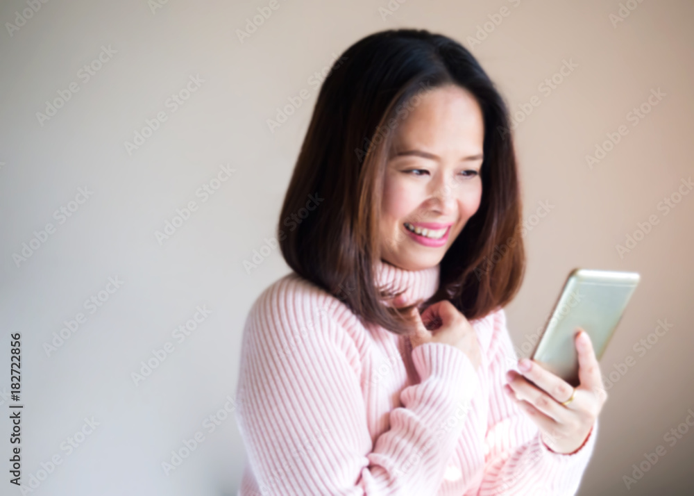 Blur portrait. Middle adult Asian woman using smart phone. Hand holding phone and smiling. Feeling happy and in love. Blur portrait. Middle adult Asian woman using smart phone. Hand holding phone and smiling. Feeling happy and in love.