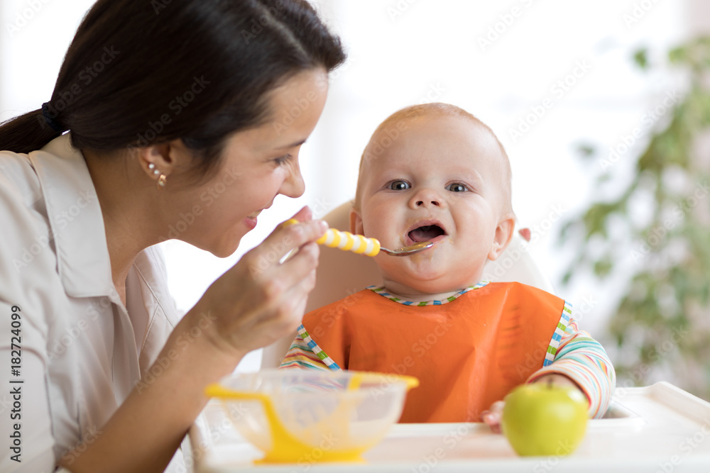 Mother feeding her baby with spoon. Mother giving healthy food to her adorable child at home Mother feeding her baby with spoon. Mother giving healthy food to her adorable child at home
