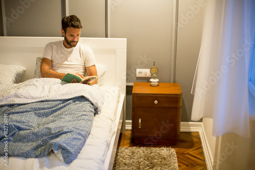 Young man reading book in bed