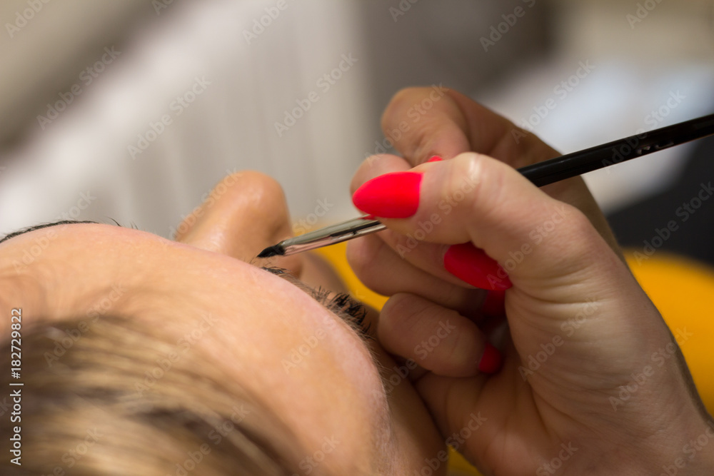 Feminine hand with a red manicure holding a brush and painting eyebrows Feminine hand with a red manicure holding a brush and painting eyebrows