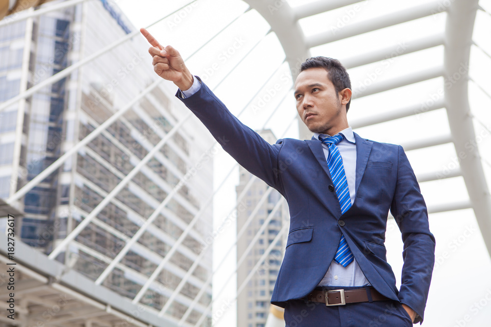 Businessman seriously and raising his fist with number 1 in the air, with office building background - business success, achievement, and win concepts Businessman seriously and raising his fist with number 1 in the air, with office building background - business success, achievement, and win concepts