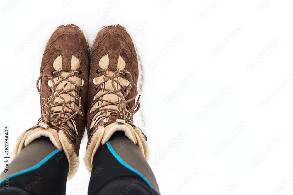 Winter warm suede brown boots with laces on the white snow with place for text.