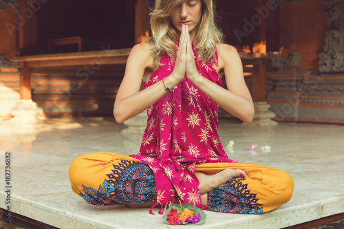 Woman practicing yoga and holding canang sari - offering for Gods. Balinese tradition.