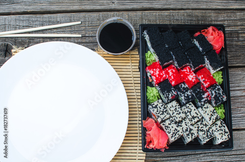 Sushi in a black container on the wooden table next to white plate photo