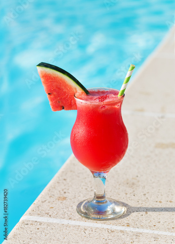 Glass of fresh watermelon smoothie juice drink on border of a swimming pool