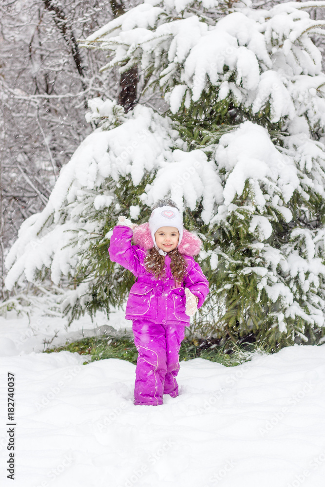 Little girl playing near the pine tree covered by snow in frosty winter weather. Little girl playing near the pine tree covered by snow in frosty winter weather.