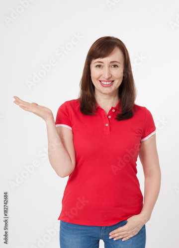 Smiling beautiful woman wearing blank red t-shirt and blue jeans and showing something by her finger, mock up on white background.