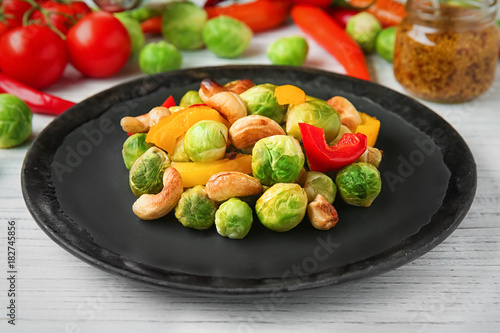 Plate with baked Brussels sprouts, pepper and nuts on table