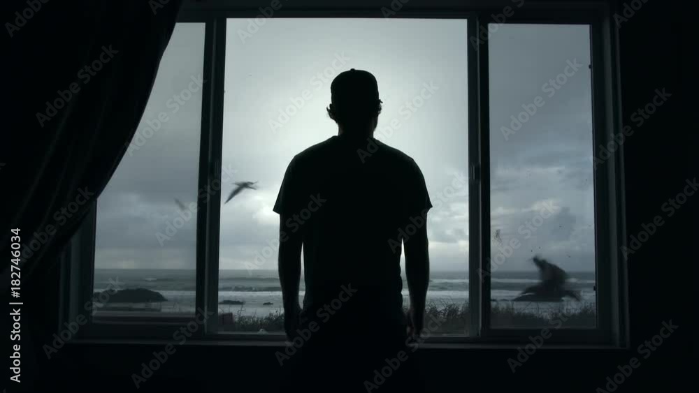 Man looks through picture window out at the ocean during stormy day on the Oregon Coast with seabirds flying by. Man looks through picture window out at the ocean during stormy day on the Oregon Coast with seabirds flying by.