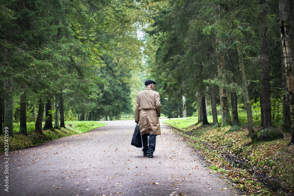 Old man in brown coat walks in park in autumn. Old man in brown coat walks in park in autumn.