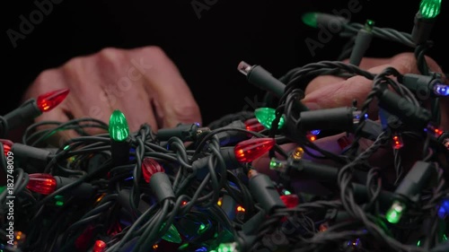 TANGLED HOLIDAY CHRISTMAS LIGHTS.  Male hands attempt to unravel.. ECU.  Version 1 of 2.