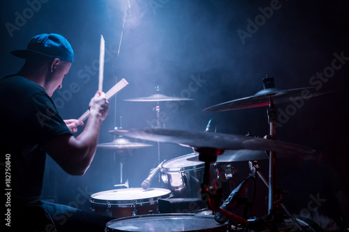 Obraz na płótnie Drummer in a cap and headphones plays drums at a concert under blue light in a s