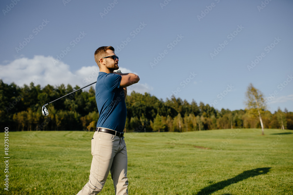 Full length view of man in cap holding golf club and hitting ball on green lawn