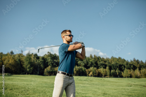 Full length view of man in cap holding golf club and hitting ball on green lawn