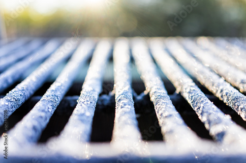 White frost ice crystals on metal grill outside in morning sunlight macro closeup with shiny sparkling bokeh