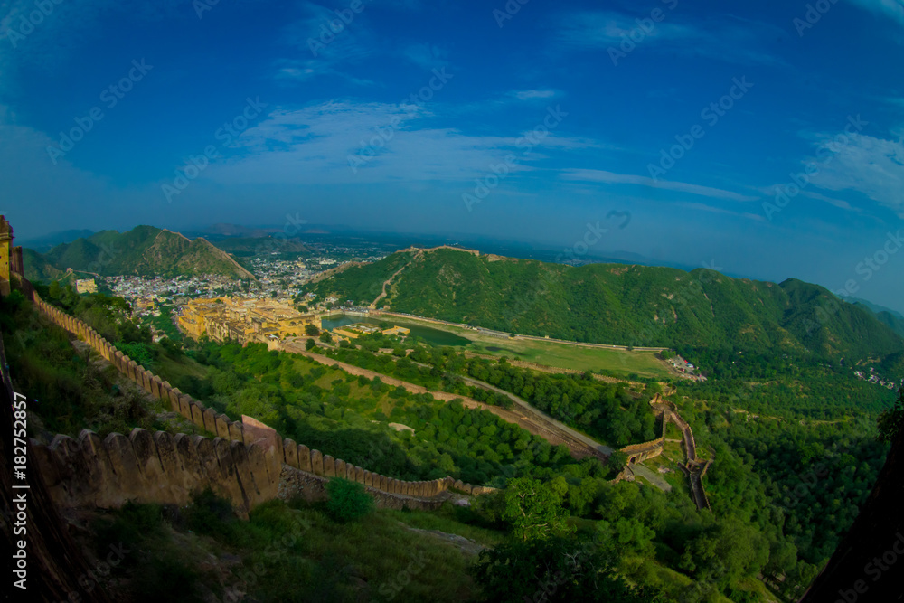 Beautiful landscape of Amber Fort with green trees, mountains and small houses near Jaipur in Rajasthan, India. Amber Fort is the main tourist attraction in the Jaipur area