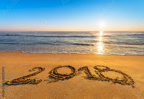 Number 2018 written on seashore sand at sunrise. Concept of upcoming new year and passing of time.