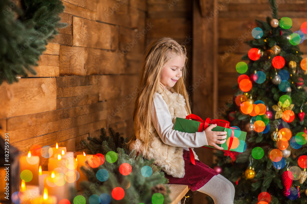 Girl, daughter, smiling, glad opens and .receives gifts on Christmas Eve or New Year near Christmas tree