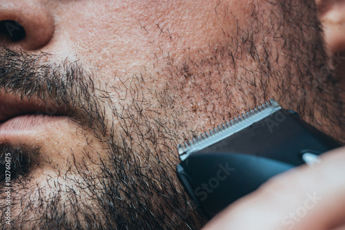 Man shaving his bristle with hair clipper or electric trimmer. Beard care and barber shop