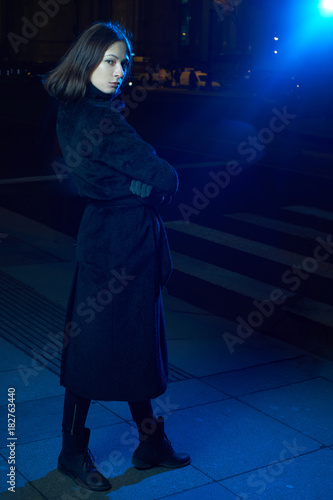 portrait of a girl in a blue backlight. in the night city. girl in a coat.