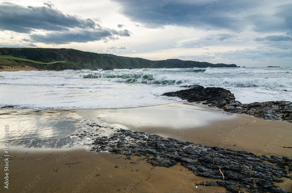 Waves on the coast in Verdicio beach in Asturias, Spain.Choppy sea in a virgin beach with rocks and foam at evening