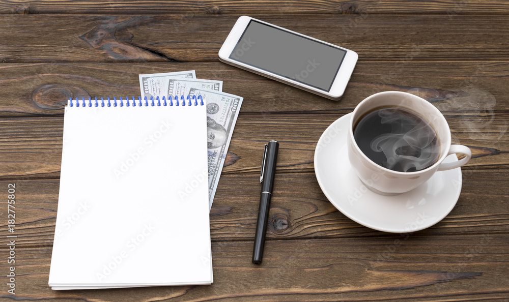 Cup of coffee, smartphone, dollars, notepad and pen on wooden desk. Cup of coffee, smartphone, dollars, notepad and pen on wooden desk.