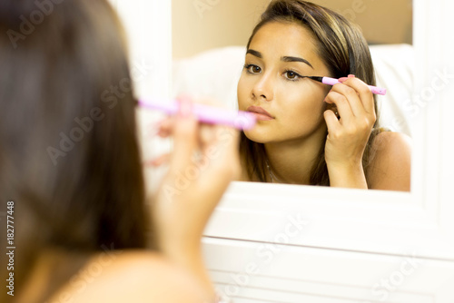 Mixed race young woman with brush eye liner on looking in the mirror