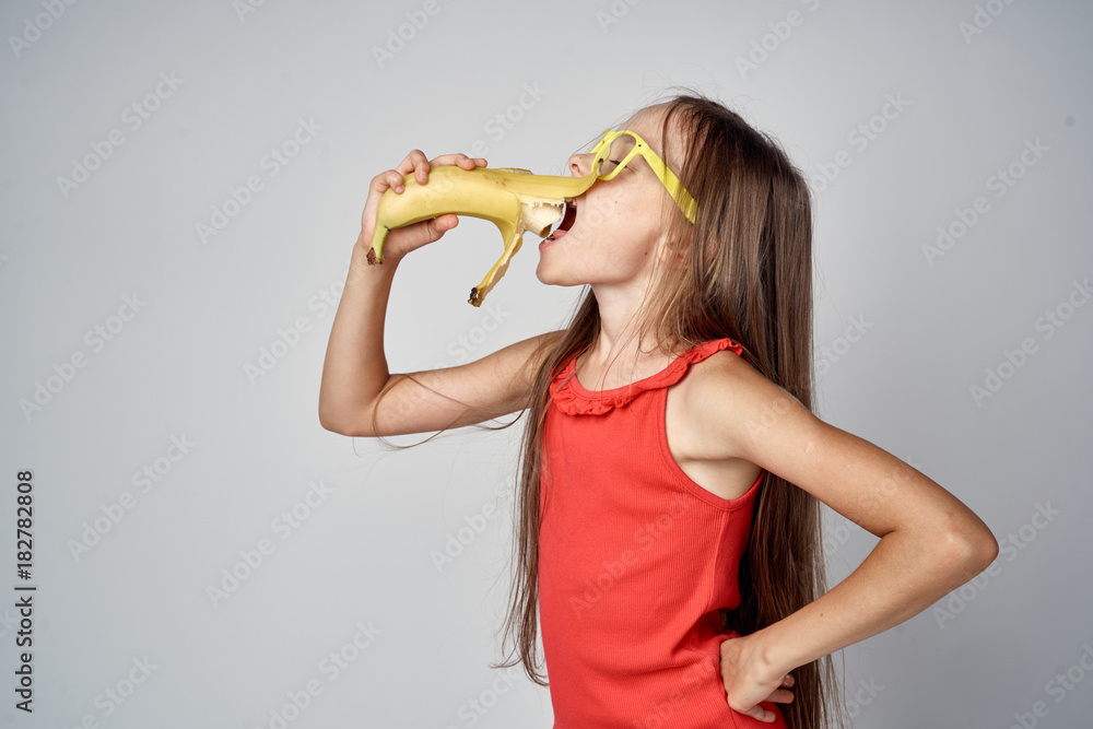 little girl in a red dress on a gray background eating a banana little girl in a red dress on a gray background eating a banana